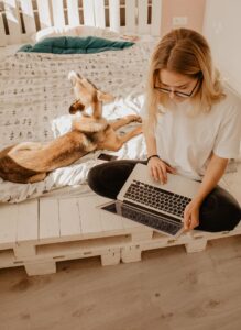 woman working on her laptop with dog on bed