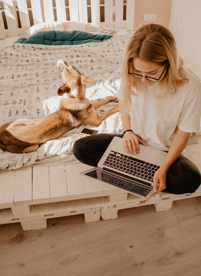woman working on her laptop with dog on bed